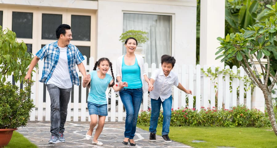 Family members walking hand-in-hand in front of a lovely home with white fencing